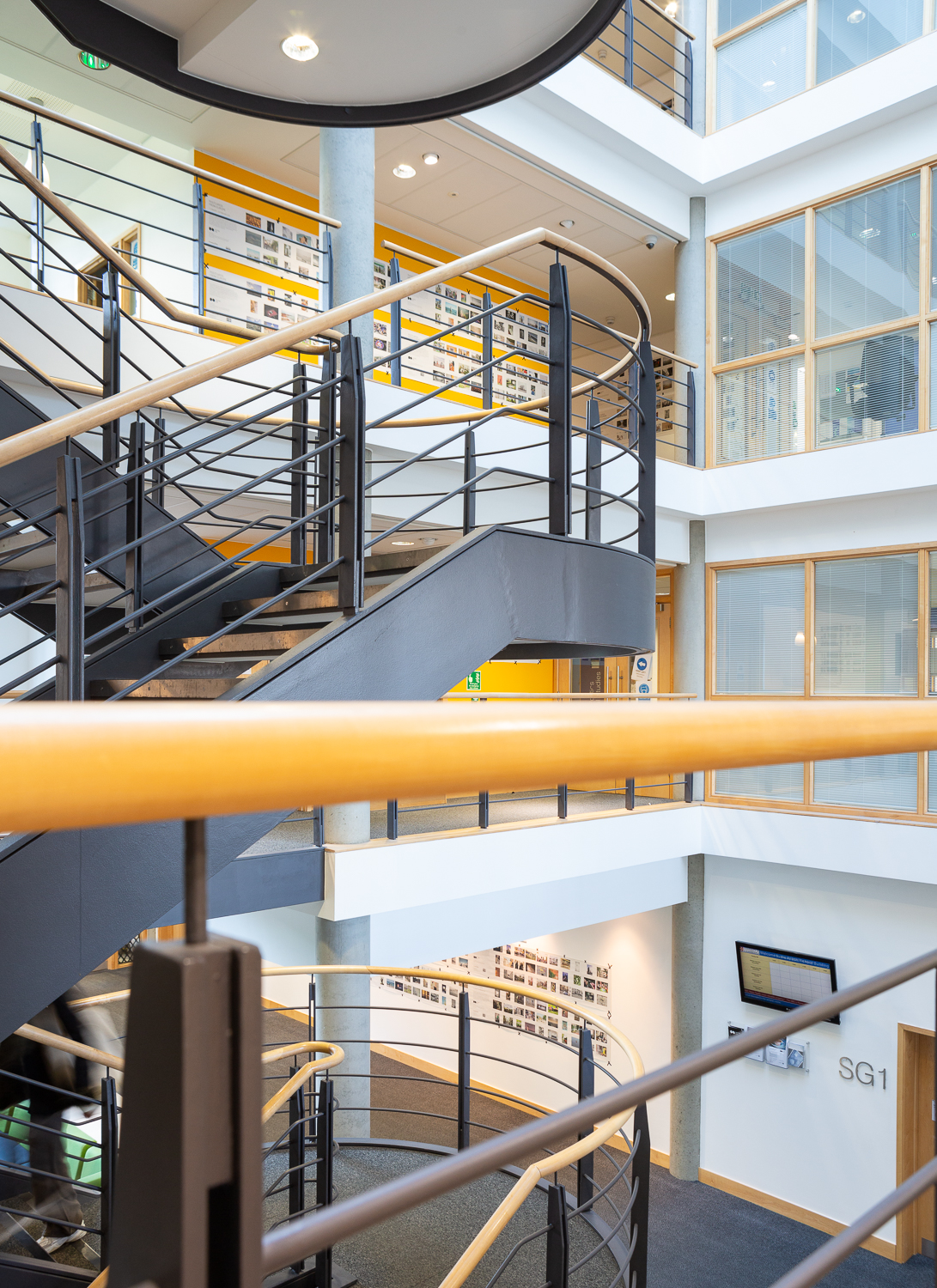 Installation photograph of 'Postcards from Europe' exhibition, postcard-sized photographs printed on long strips of newsprint, displayed across different floors of Art at the ARB, with a staircase featured in the middle of the building.