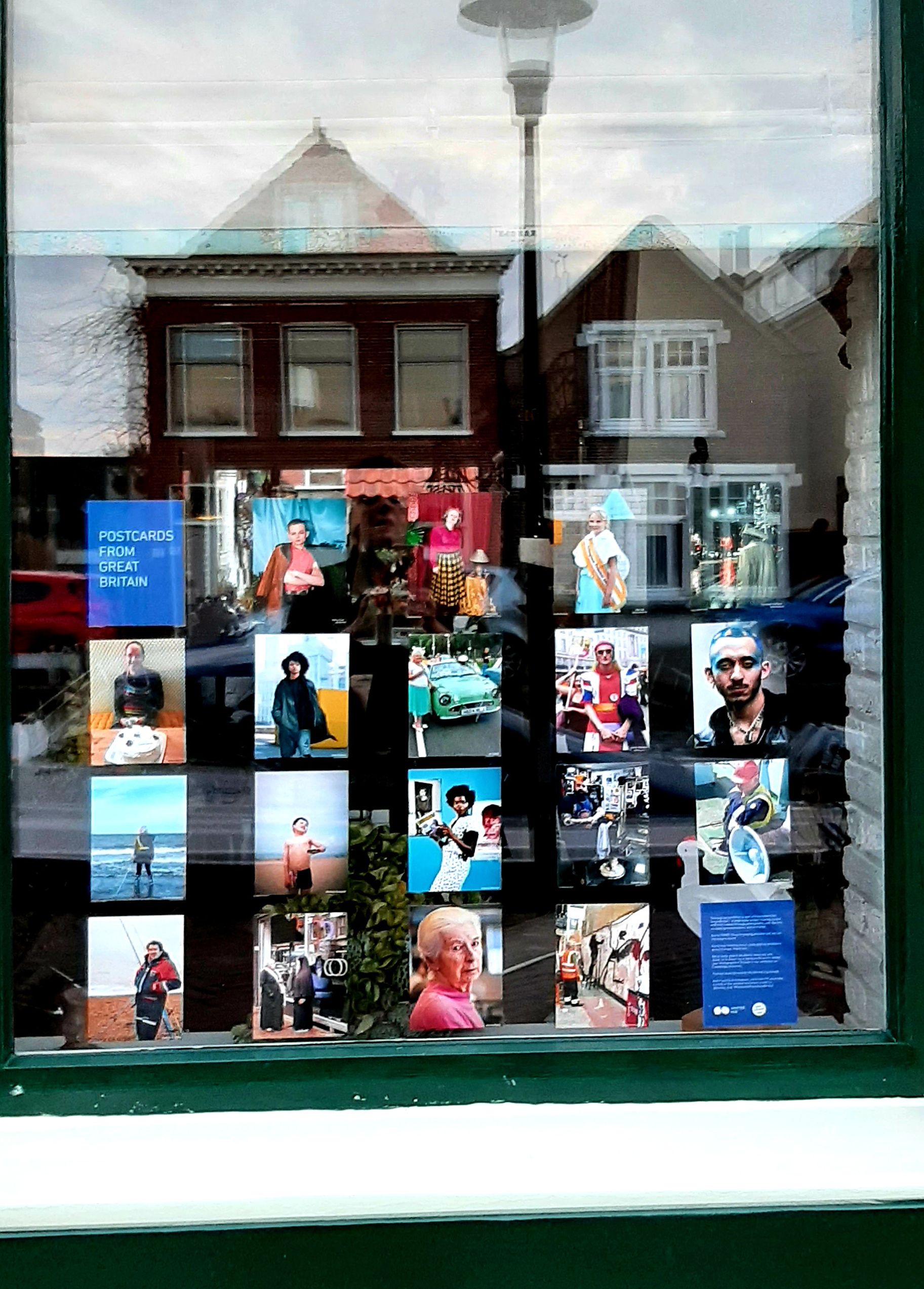 Photograph of a window displaying postcard-sized photographs, with buildings reflected in the top of the window.