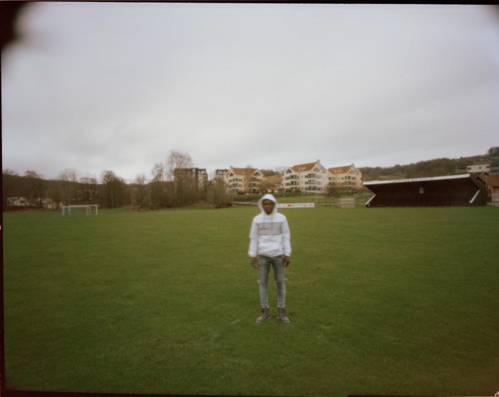 An out of focus refugee photographed in a green field but the weather is overcast and cold.