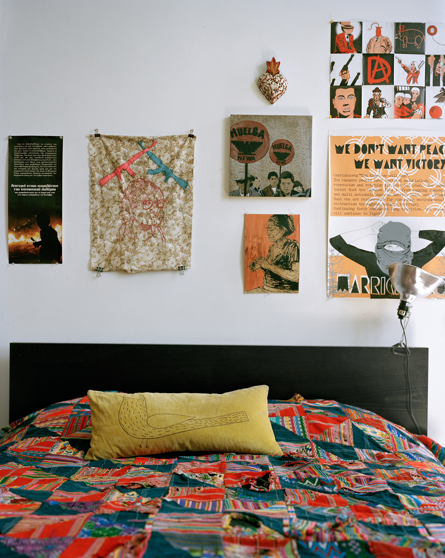 Close up of a bed with a colourful cover against a wall filled with posters, artworks and drawings.