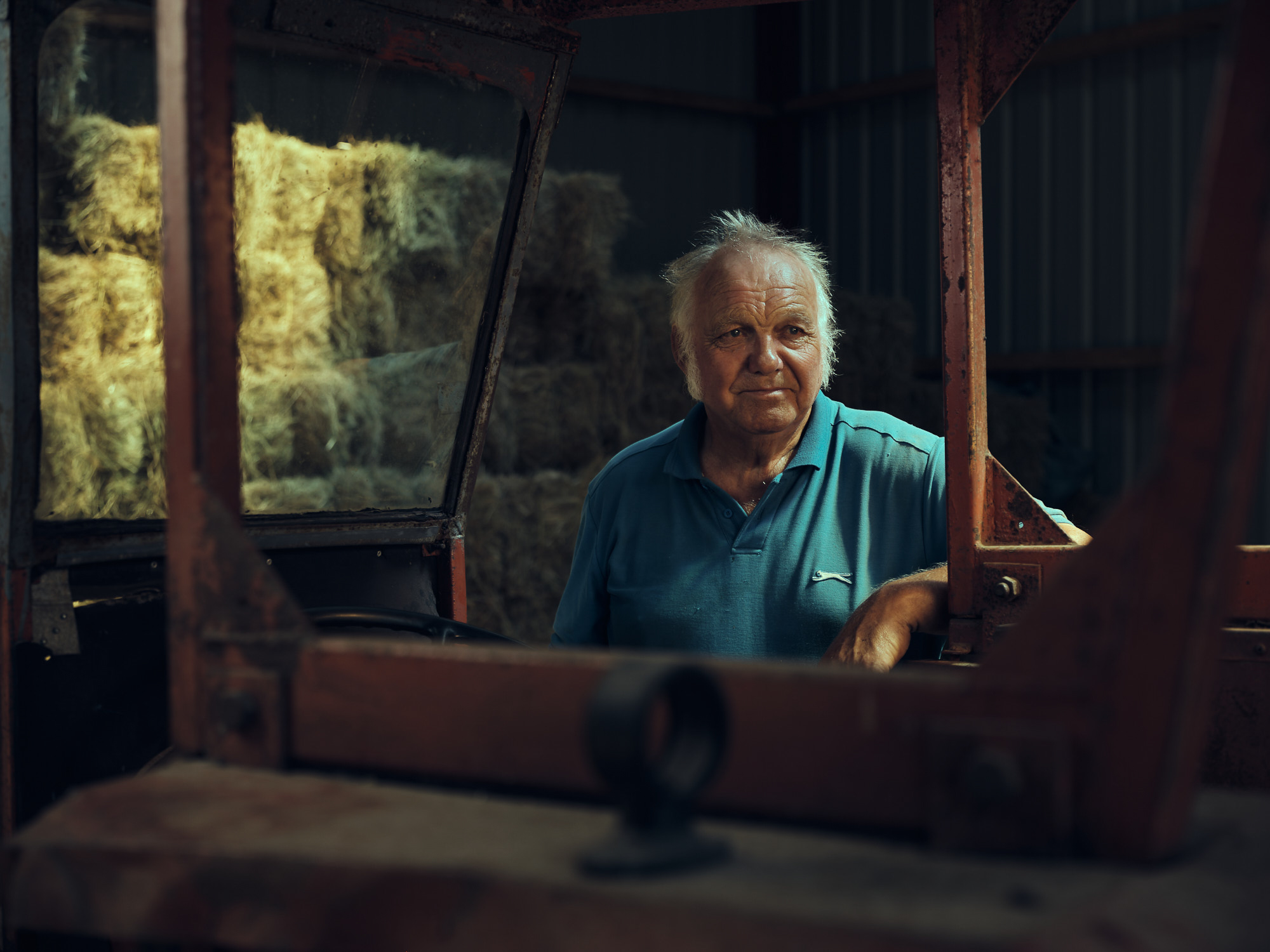 A farmer stands beside his red tractor in a hay shed.