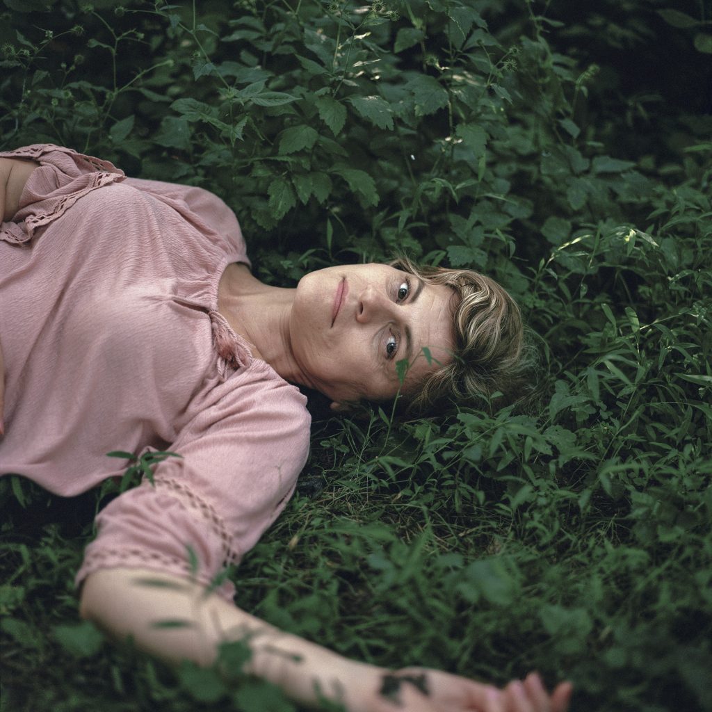 Photographic portrait of reclining women on green grass, with blonde hair and pink blouse