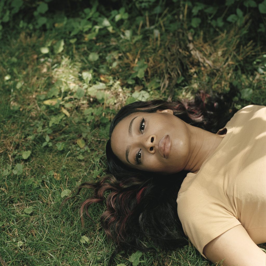 Photographic portrait of reclining women on green grass with dark hair and yellow blouse