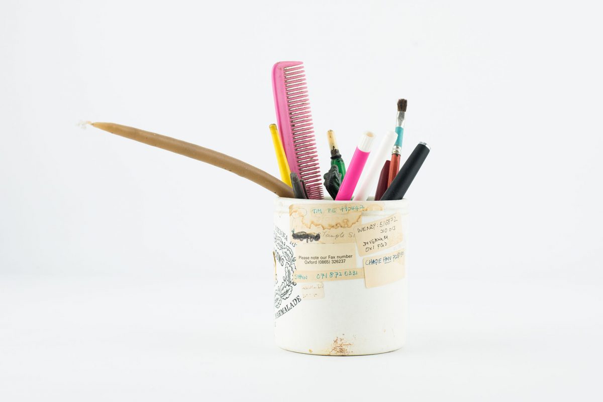 white container filled with pencils, brushes and a pink comb, white background