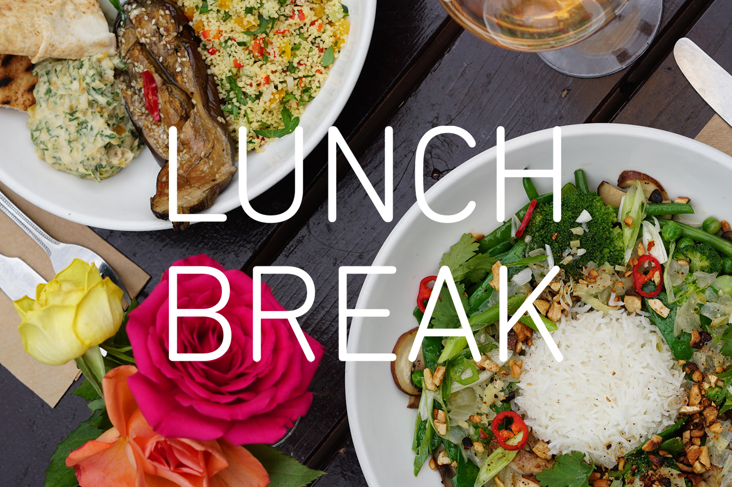 plates with food on a brown wooden table, next to roses, with 'LUNCH BREAK' written in white in the centre